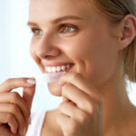 A woman applying teeth whitening strips.